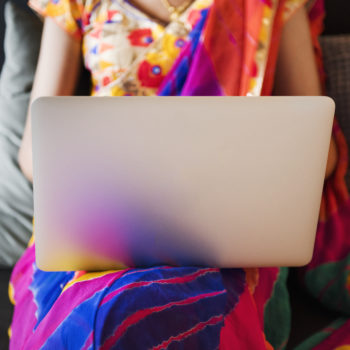 Woman in colorful sari reads a blog on her laptop.