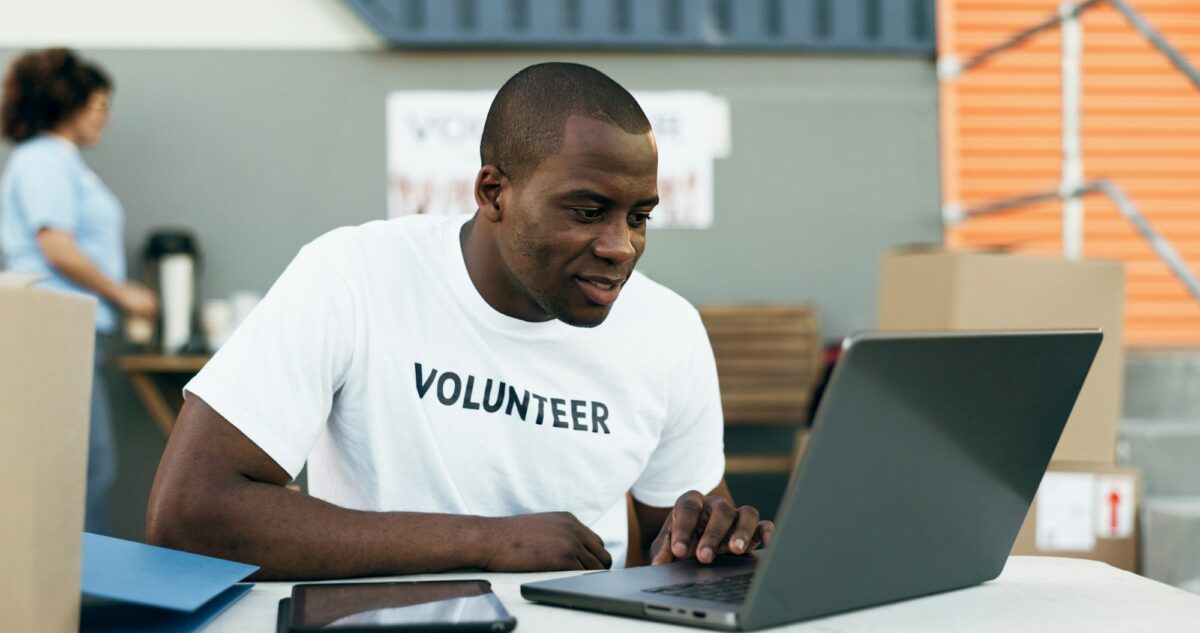 Volunteer man, laptop and reading for donation, clothes drive and smile for community service, scro