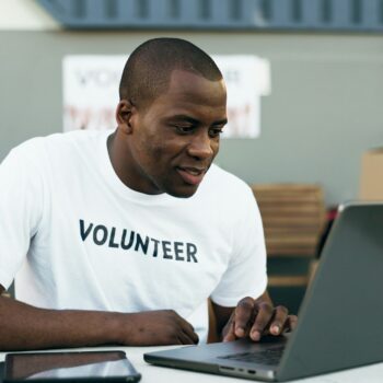 Volunteer man, laptop and reading for donation, clothes drive and smile for community service, scro