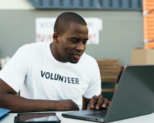 Volunteer man, laptop and reading for donation, clothes drive and smile for community service, scro