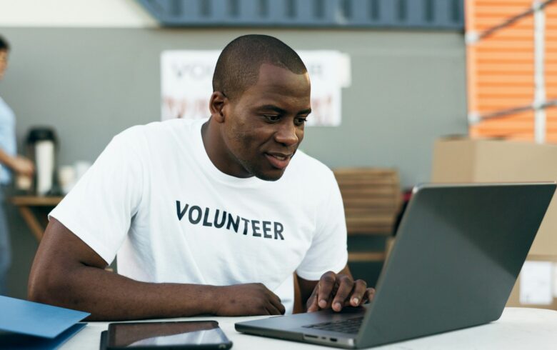 Volunteer man, laptop and reading for donation, clothes drive and smile for community service, scro